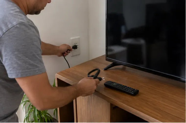 Pessoa desconectando o cabo de energia de uma televisão antes do descarte