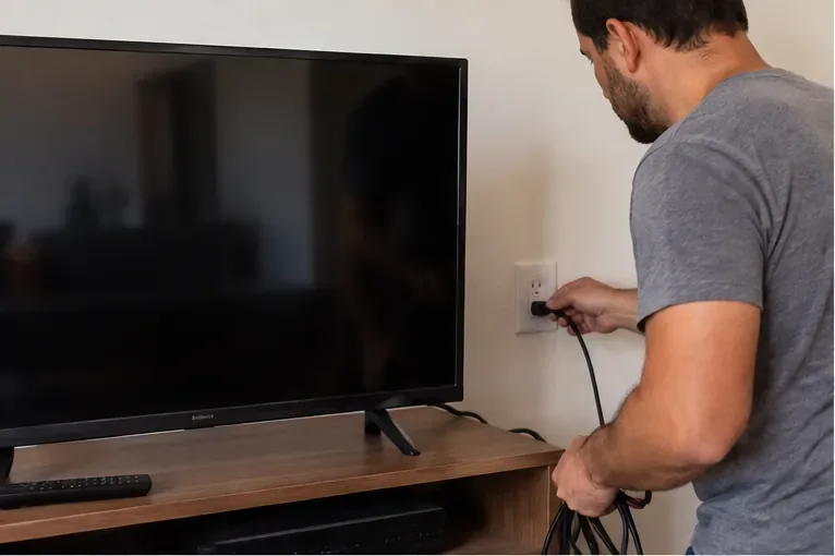 Homem desconectando da tomada uma televisão de tela plana antes do descarte