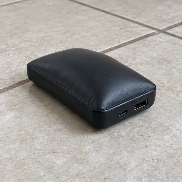 Power bank preto com a carcaça abaulada, desligado, sobre um piso cerâmico seco.