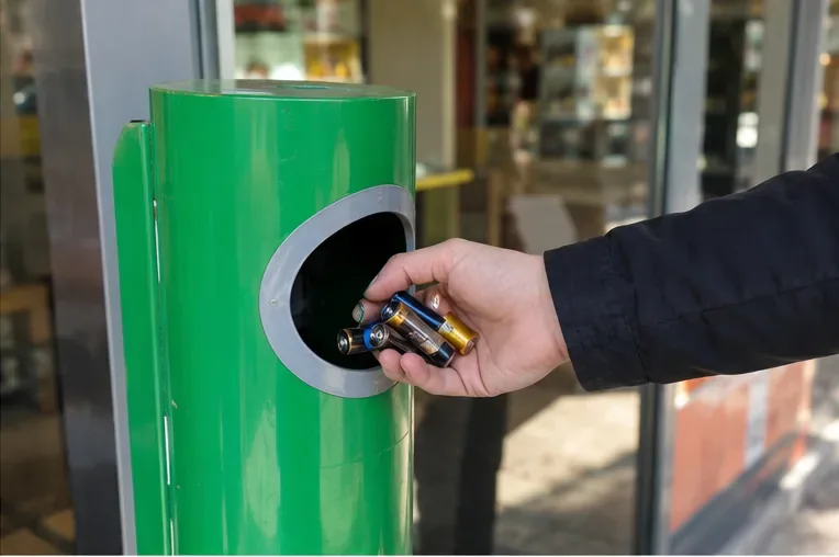 Una mano introduce varias pilas cilíndricas usadas en un contenedor específico de recogida