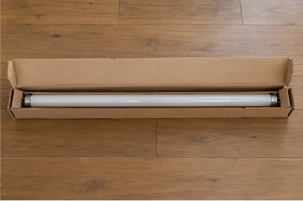 Un tubo fluorescente intacto está colocado recto dentro de una caja larga de cartón, con protección en los extremos.