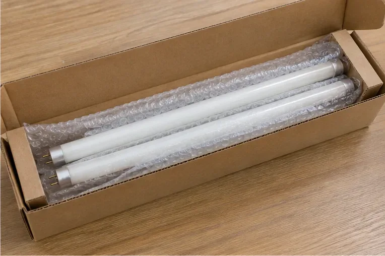 Dos tubos fluorescentes lineales protegidos dentro de una caja de cartón alargada con material de amortiguación