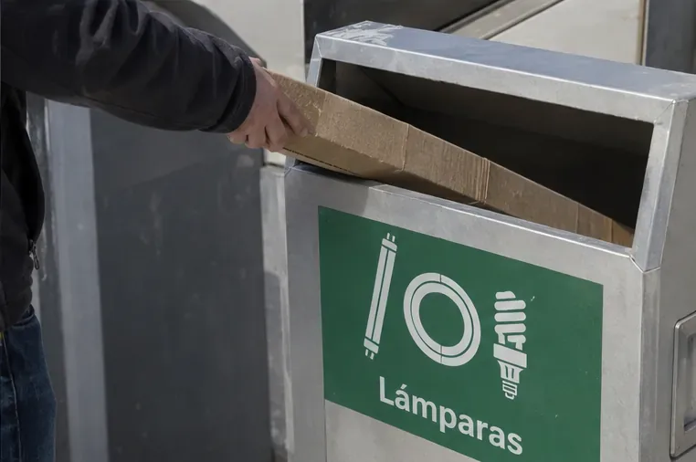 Persona introduciendo con cuidado un tubo fluorescente protegido en un contenedor señalizado para lámparas