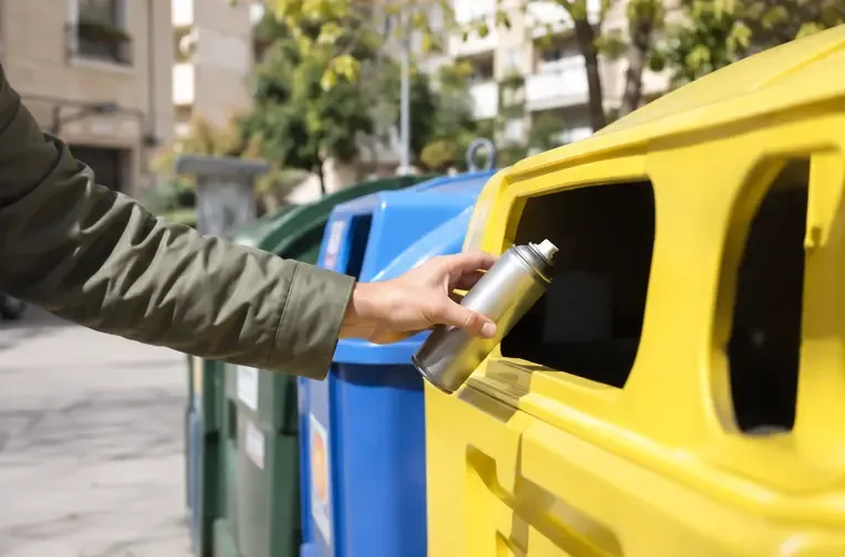 Una lata de aerosol completamente vacía e intacta se deposita en un contenedor amarillo de envases