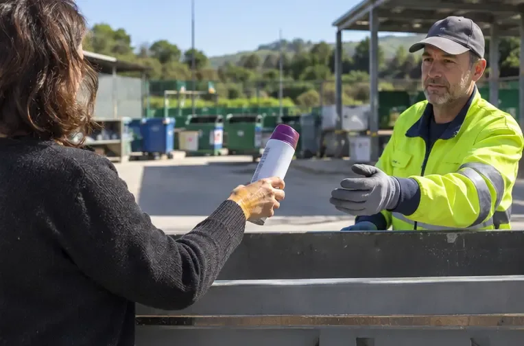 Una persona entrega un aerosol con producto a un trabajador con guantes en un ecoparque municipal genérico
