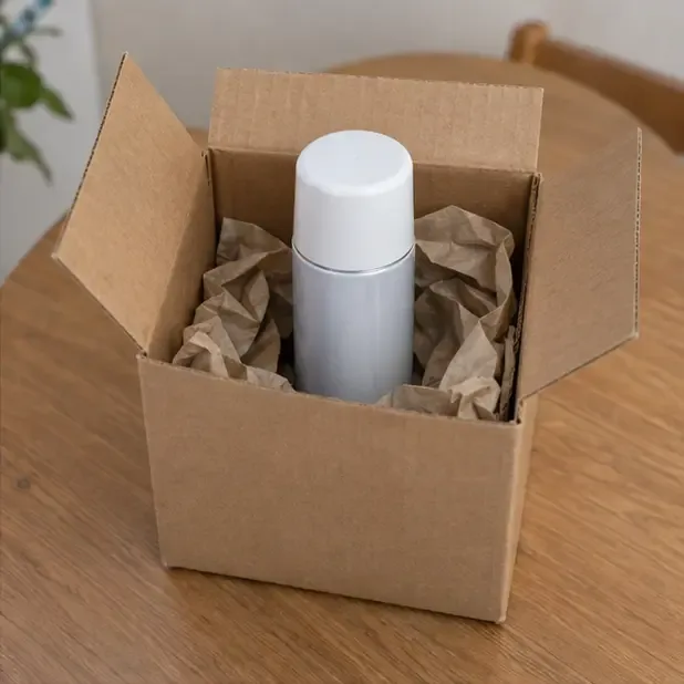 Aerosol doméstico con tapón colocado y en posición vertical dentro de una caja de cartón con protección de papel