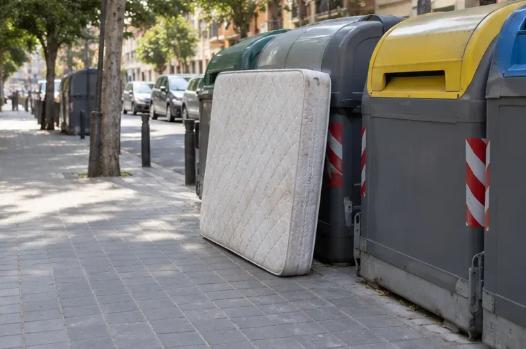 Un colchón colocado de forma vertical junto a una batería de contenedores sin ocupar el centro de la acera