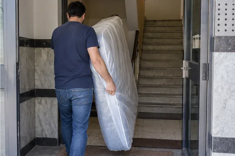 Una persona transporta un colchón protegido mientras atraviesa la entrada de un edificio residencial