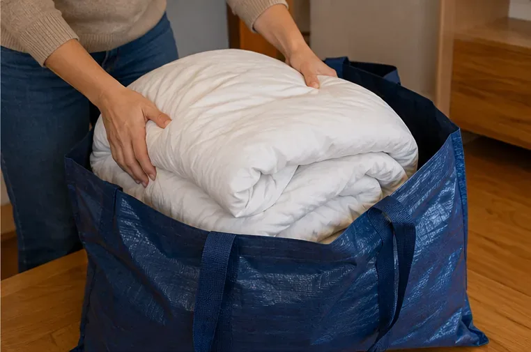Manos doblando un edredón blanco e introduciéndolo en una bolsa azul grande y resistente