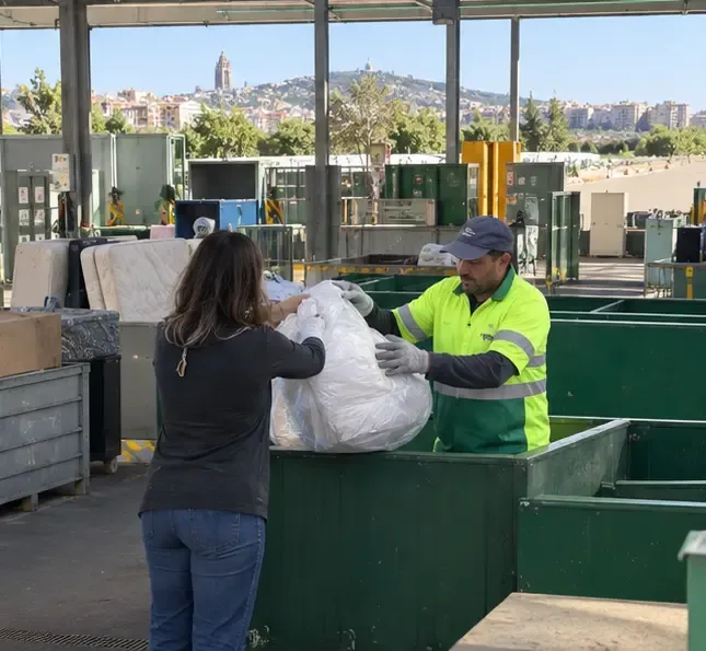 Una trabajadora recibe una bolsa con un edredón en una instalación municipal de recogida de residuos