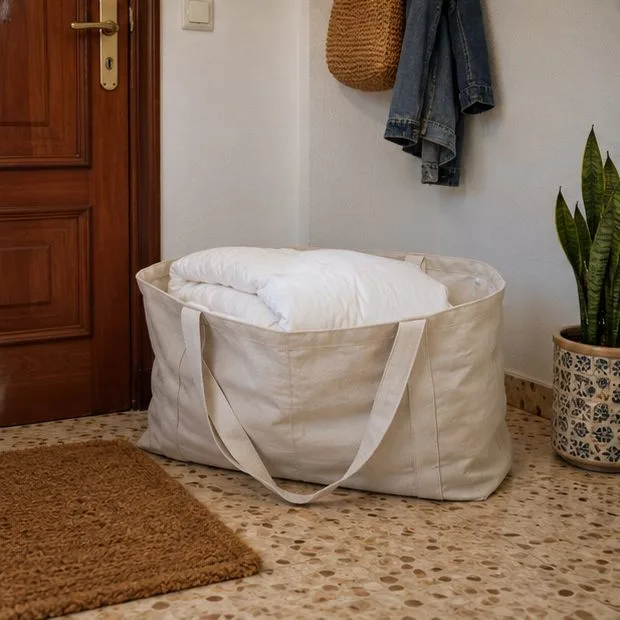 Un edredón blanco doblado dentro de una bolsa de tela colocada en la entrada de una vivienda.
