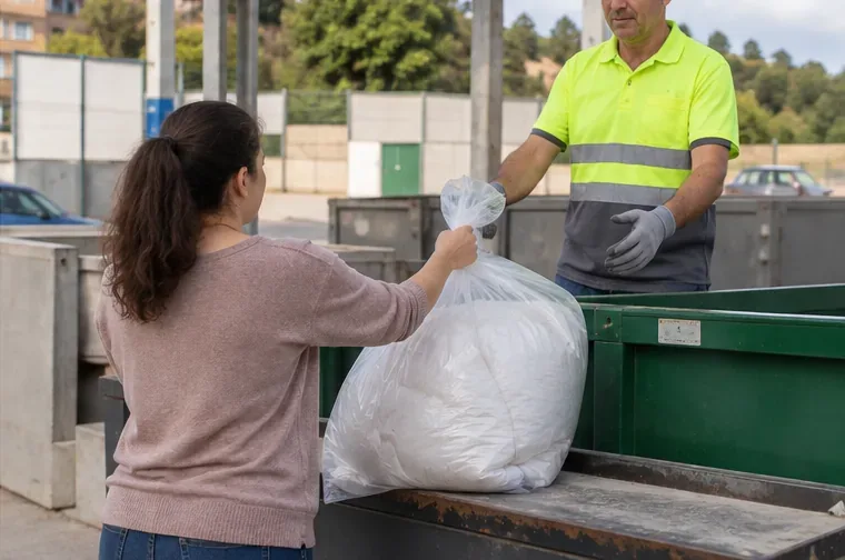 Persona entregando una bolsa con un edredón a un operario en una instalación de recogida de residuos