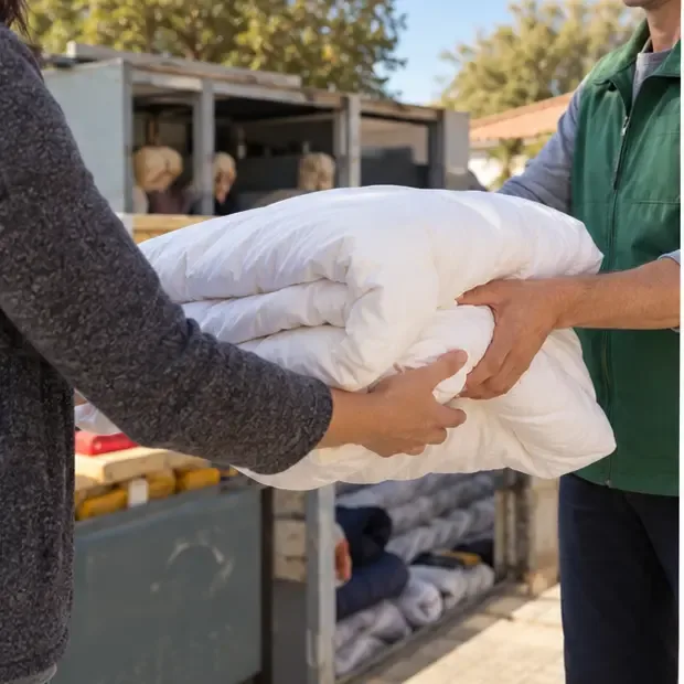 Dos personas entregando un edredón doblado en un punto neutral de reutilización textil