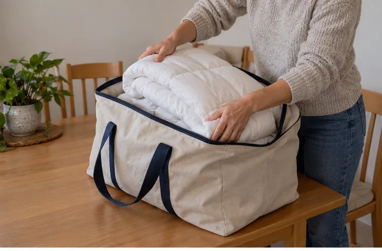 Las manos doblan un edredón blanco y lo guardan en una bolsa grande de tela sobre una mesa