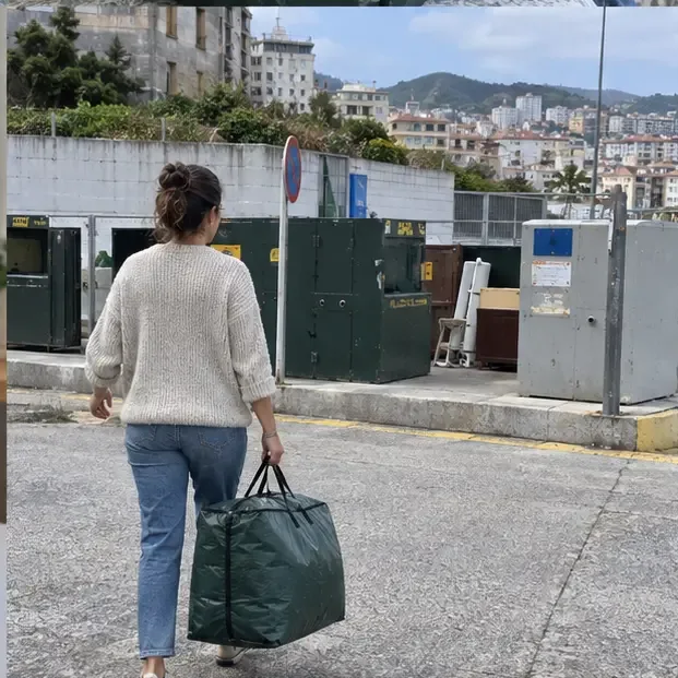 Persona llevando una bolsa cerrada con un edredón hacia una zona urbana de recogida de residuos en Vigo