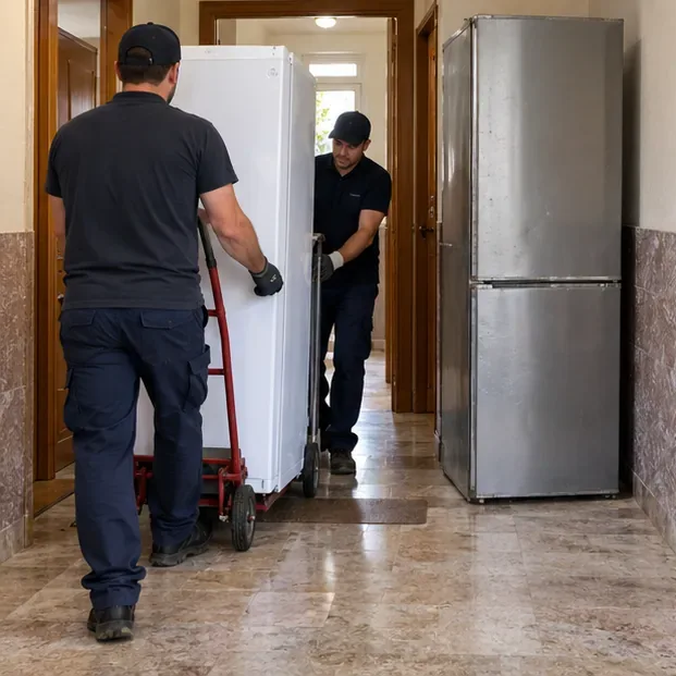 Dos repartidores desplazan un frigorífico antiguo con una carretilla por el pasillo mientras entregan un aparato nuevo.