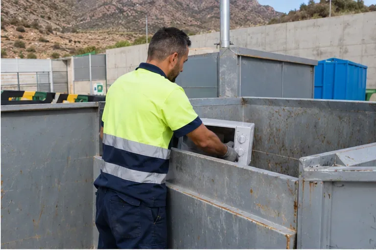 Un operario coloca un microondas en un área de recepción de residuos separada.