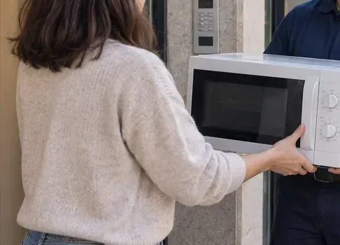 Persona entregando un microondas de sobremesa a un trabajador en la entrada de un edificio