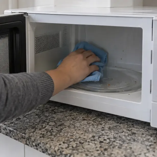 Una persona limpia el interior vacío de un microondas abierto con un paño