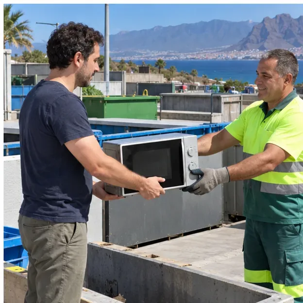 Un vecino entrega un microondas a un trabajador con guantes en una instalación municipal de reciclaje.