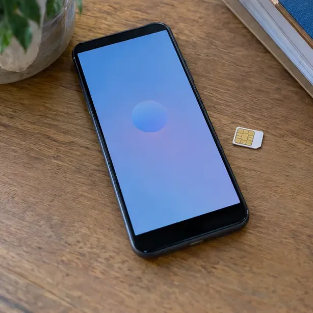 Teléfono móvil sobre una mesa mostrando una pantalla genérica sin datos personales junto a una tarjeta SIM retirada