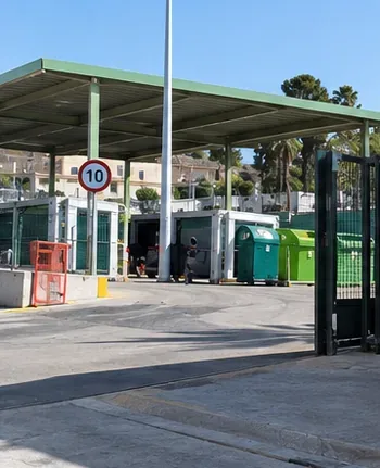 Acceso abierto a un recinto de recogida con contenedores separados bajo una cubierta.