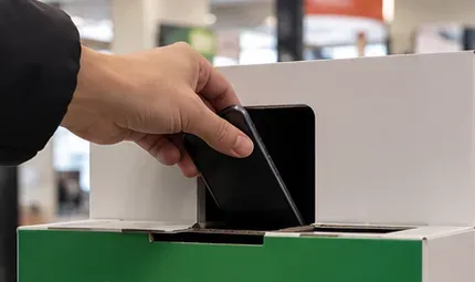 Una mano introduce un teléfono en la abertura de un recipiente de recogida sobre un mostrador.