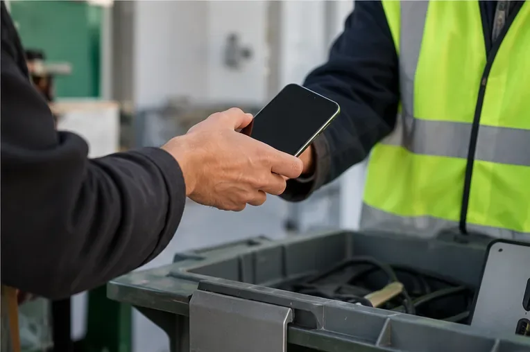 Persona entregando un teléfono móvil a un trabajador de un punto de recogida de residuos electrónicos