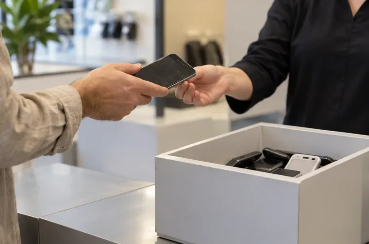 Una persona entrega un teléfono usado a otra persona junto a un recipiente de recogida de aparatos electrónicos