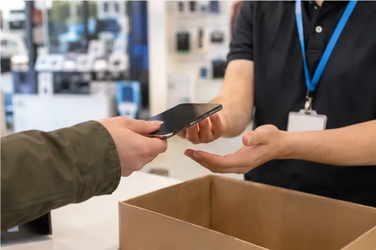 Cliente entregando un teléfono móvil usado a un empleado en el mostrador de una tienda de electrónica
