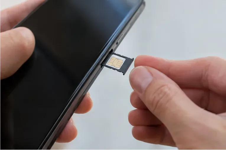 Manos retirando la bandeja con tarjeta SIM de un teléfono móvil antes de entregarlo para reciclaje