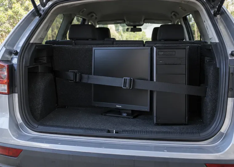 Una torre y un monitor sujetos con una cincha dentro del maletero de un coche para su traslado
