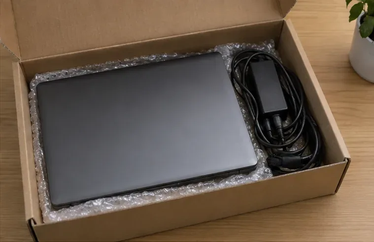 Portátil apagado y cargador colocados de forma protegida en una caja para transportarlos a un punto de recogida