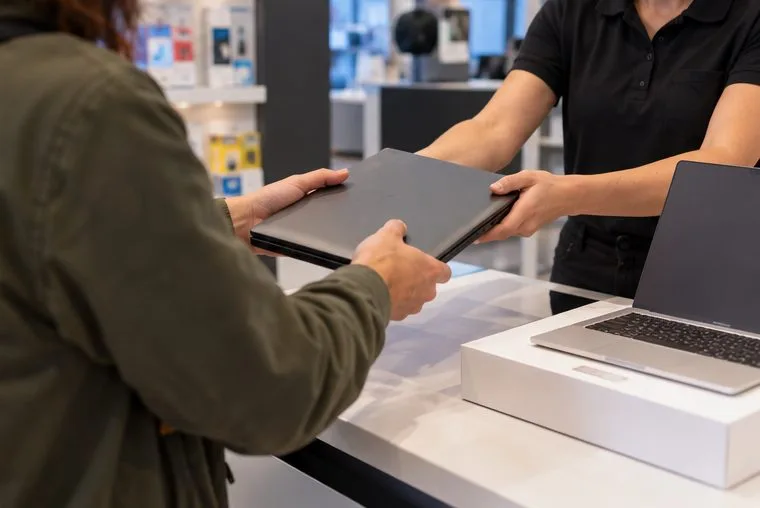 Cliente entregando un portátil antiguo al personal de una tienda de informática al comprar un equipo nuevo
