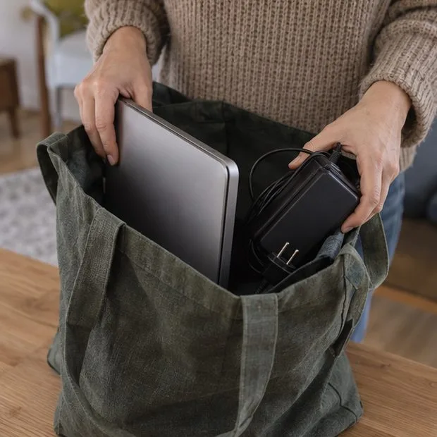 Una persona coloca un portátil cerrado y su cargador en una bolsa para trasladarlos.