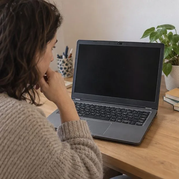 Una mujer sentada ante un portátil abierto con la pantalla apagada, en un escritorio doméstico.
