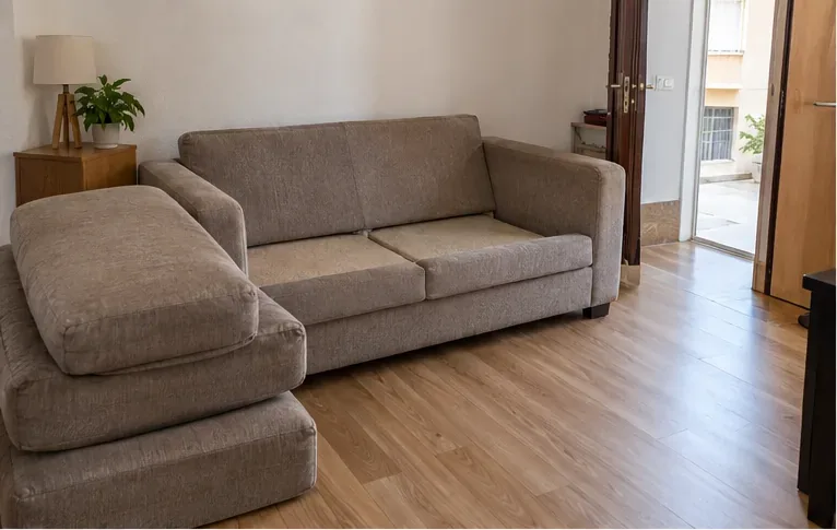 Sofá de tela en una vivienda con los cojines retirados y apilados antes de organizar su retirada