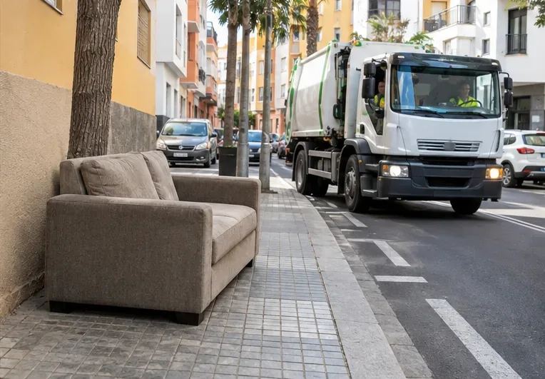 Sofá colocado junto a una fachada urbana mientras se aproxima un camión de recogida