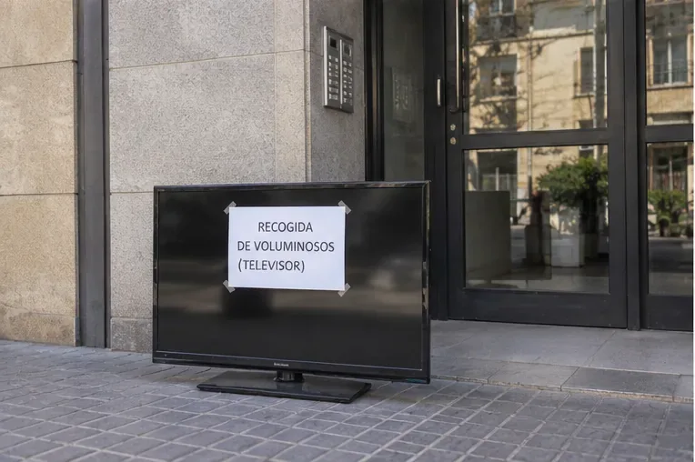 Televisor preparado junto a la entrada de un edificio con un cartel que indica recogida de voluminosos