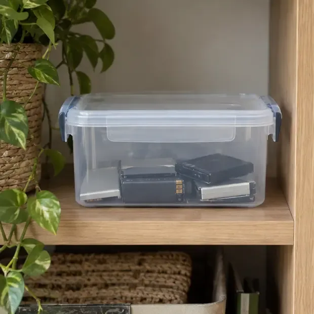 Caja de plástico con tapa que contiene varias baterías usadas en un lugar fresco y seco del hogar