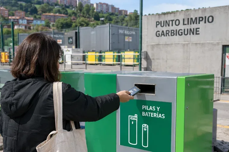 Persona depositando una batería en un contenedor específico de pilas y baterías frente a un punto limpio o Garbigune