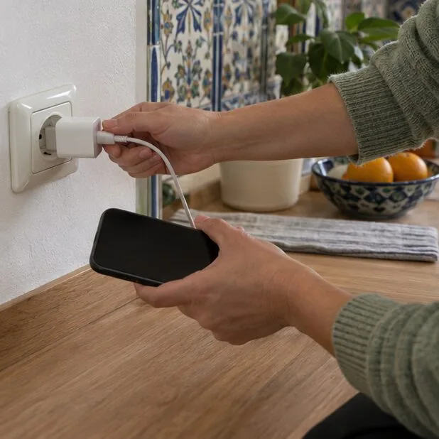 Manos desconectando un cargador de la pared mientras sostienen un dispositivo portátil