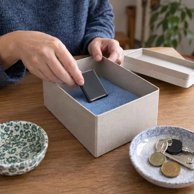 Una persona coloca una batería plana en una caja de cartón, separada de un pequeño cuenco con monedas y llaves
