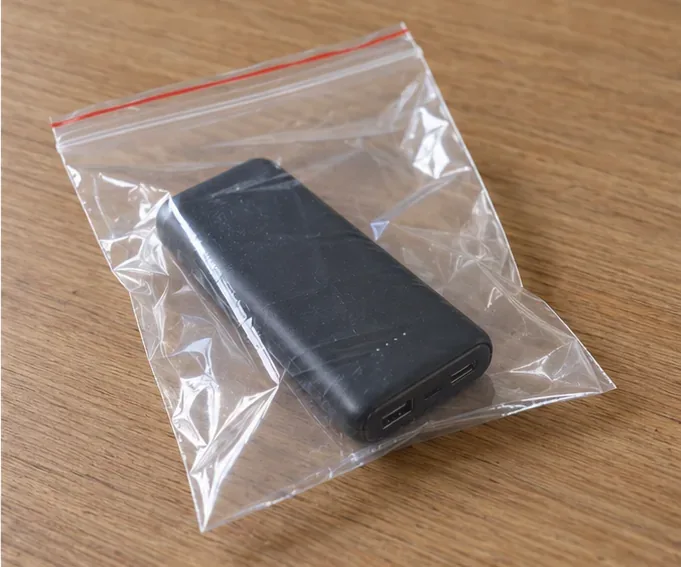 Una batería externa negra colocada sola dentro de una bolsa transparente sobre una mesa de madera