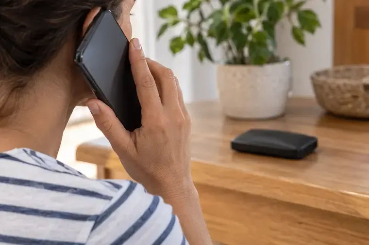 Persona llamando por teléfono mientras una batería externa hinchada permanece apartada sobre una mesa