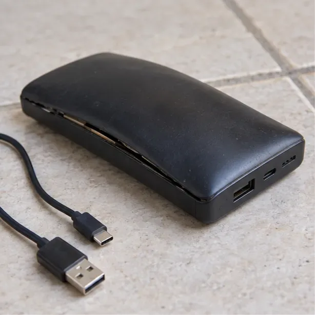 Batería externa con la carcasa abombada sobre suelo cerámico; el cable está desconectado y nadie la manipula.