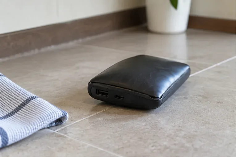 Batería externa negra visiblemente abombada colocada sobre una superficie cerámica, lejos de aparatos conectados