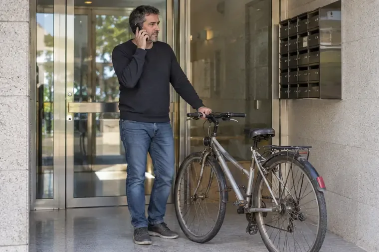 Una persona habla por teléfono junto a una bicicleta en la entrada de un edificio residencial