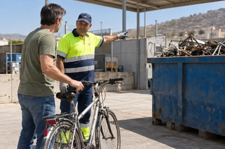Trabajador con ropa de alta visibilidad indicando a una persona dónde entregar una bicicleta usada en una zona de reciclaje