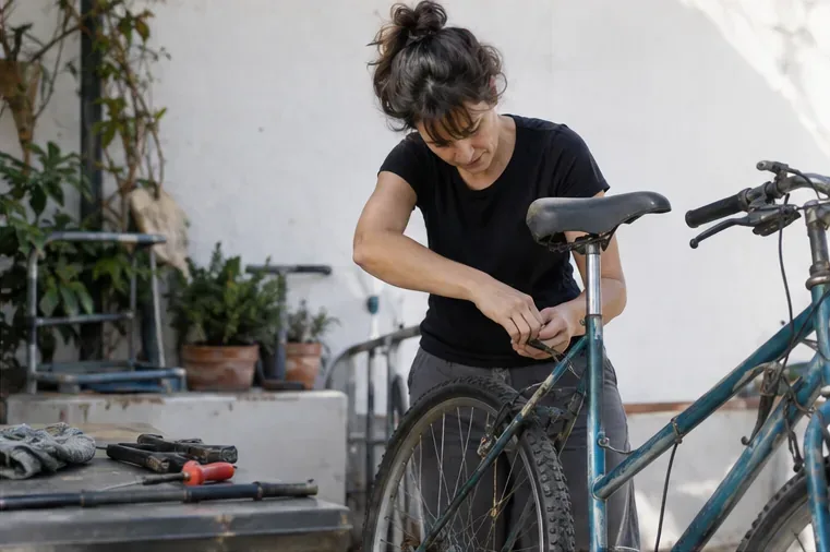 Persona retirando con una herramienta un accesorio de una bicicleta vieja junto a piezas y trapos de taller